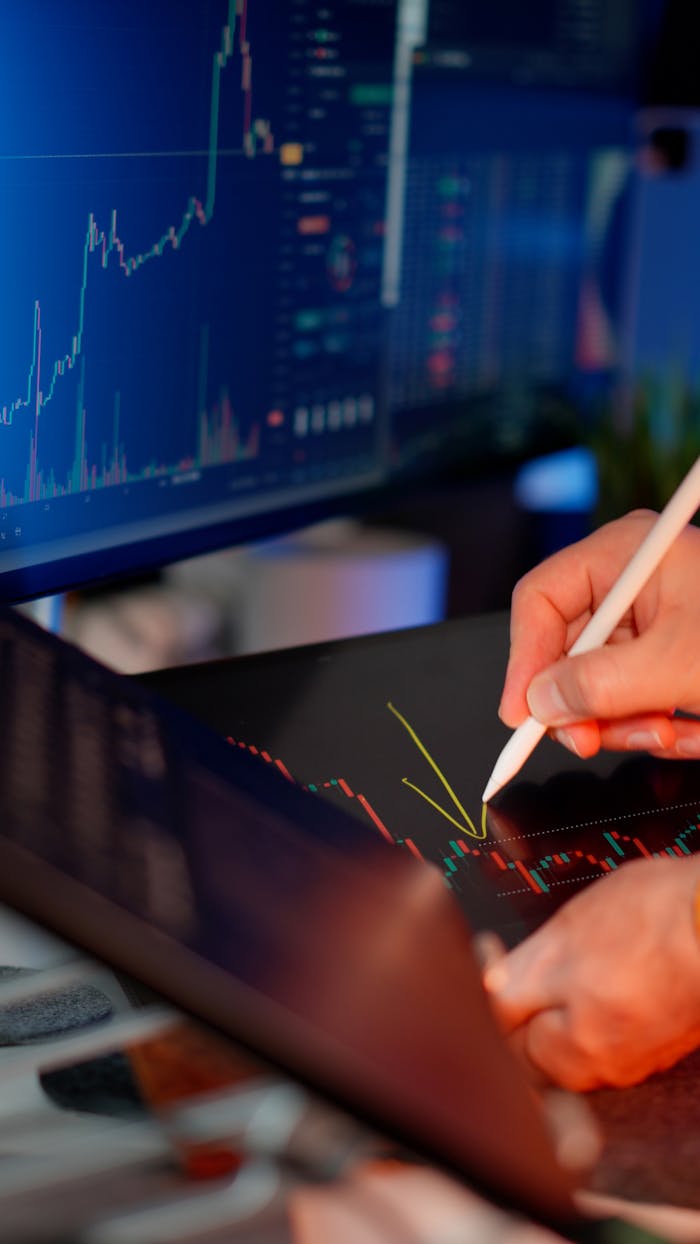 services-03 Person using a stylus on a tablet for stock market analysis, with charts on a monitor.
