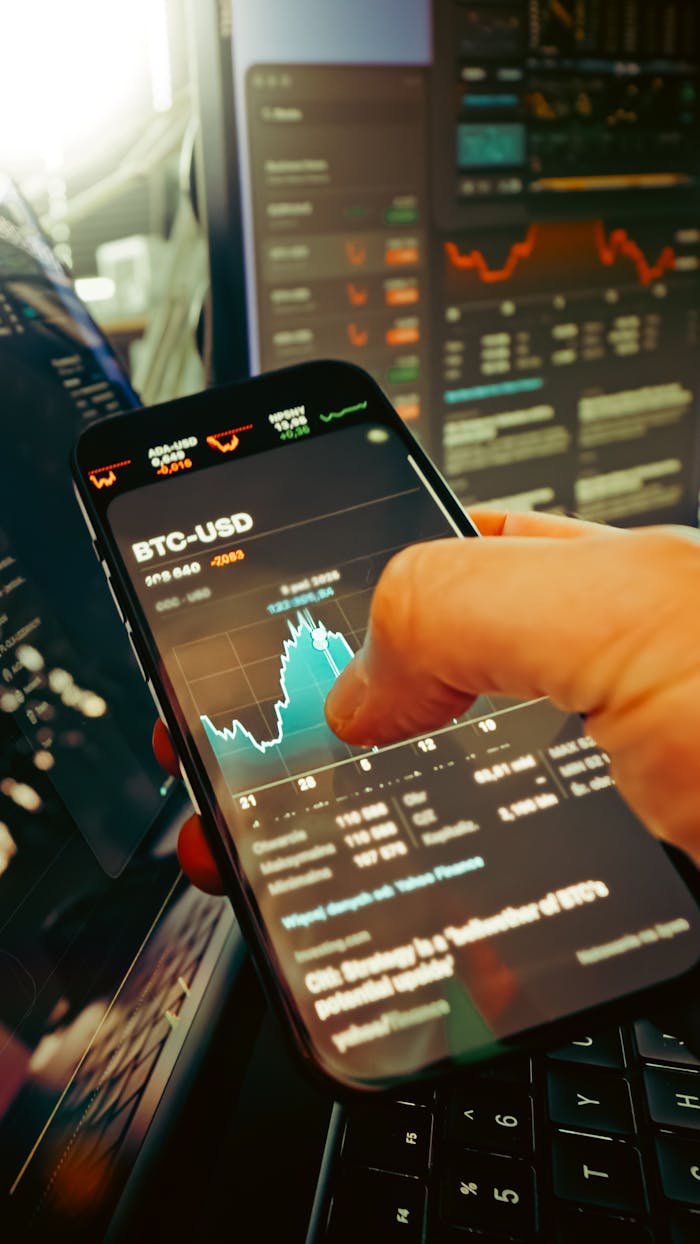 services-02 A hand holds a smartphone displaying BTC-USD chart amidst digital trading screens, highlighting crypto finance.