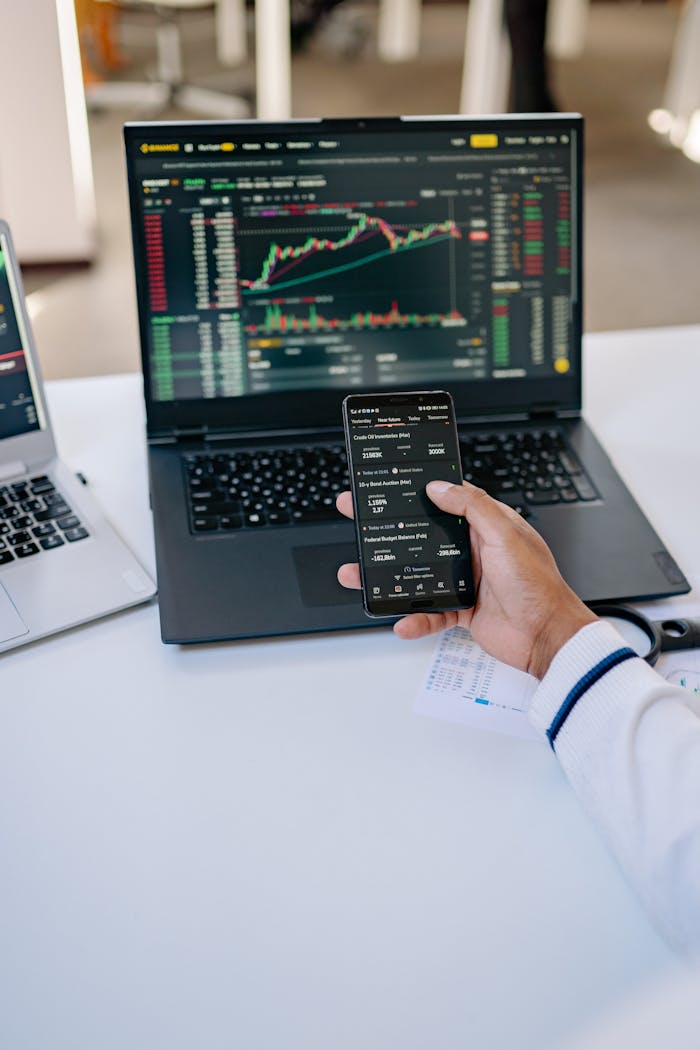 portfolio-08 Person analyzing stock market data on a laptop and smartphone at a desk.