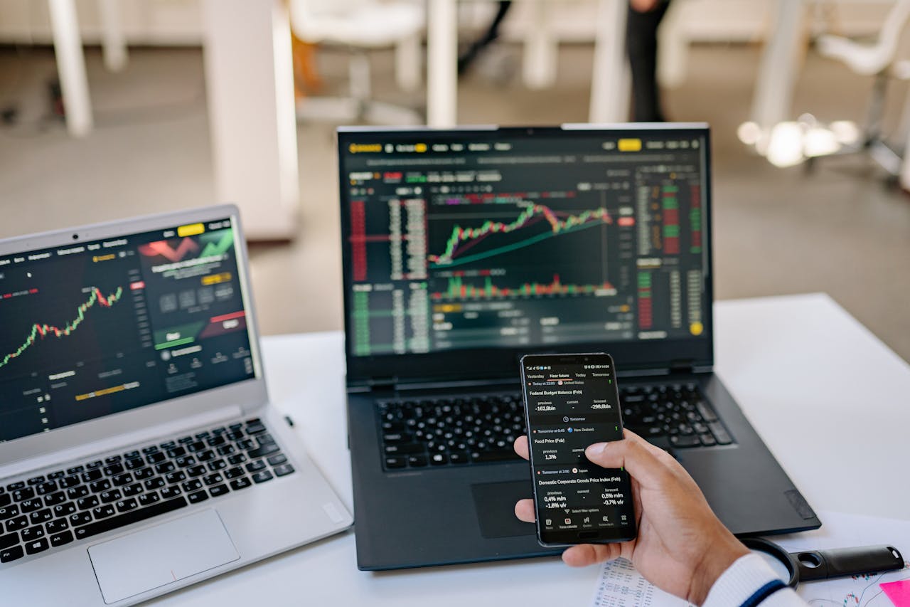 portfolio-01 A professional tracks stock market trends using two laptops and a smartphone, showcasing digital finance tools.