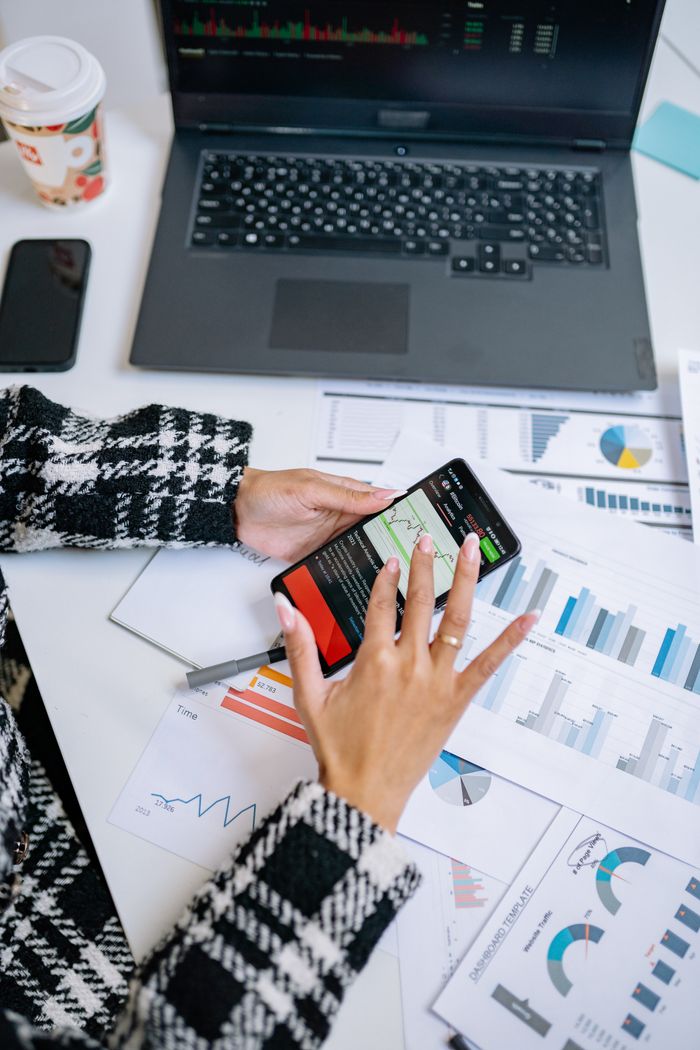 portfolio-05 Person analyzing business charts with smartphone and laptop on desk.