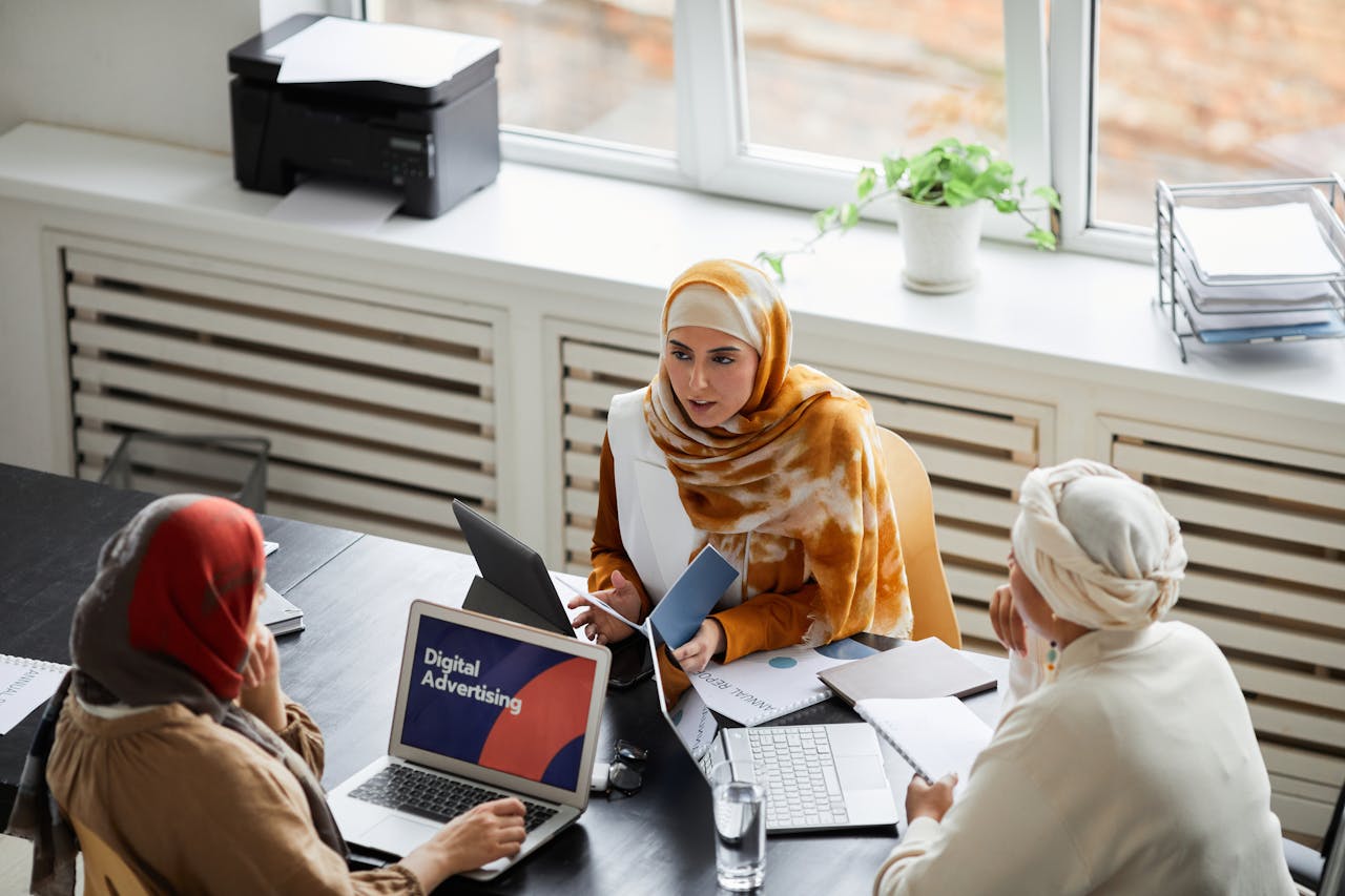 portfolio-06 Three businesswomen in hijabs discussing digital advertising at an office table.