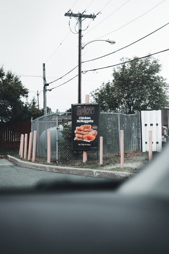 about-01 Outdoor signage featuring Spicy Chicken McNuggets beside a chain link fence and electric post.
